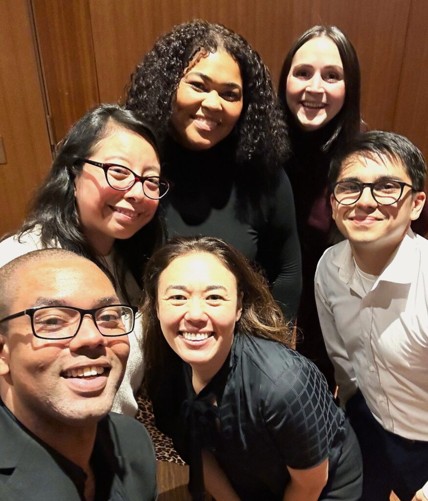Group of six people smiling together for a photo at an indoor event.