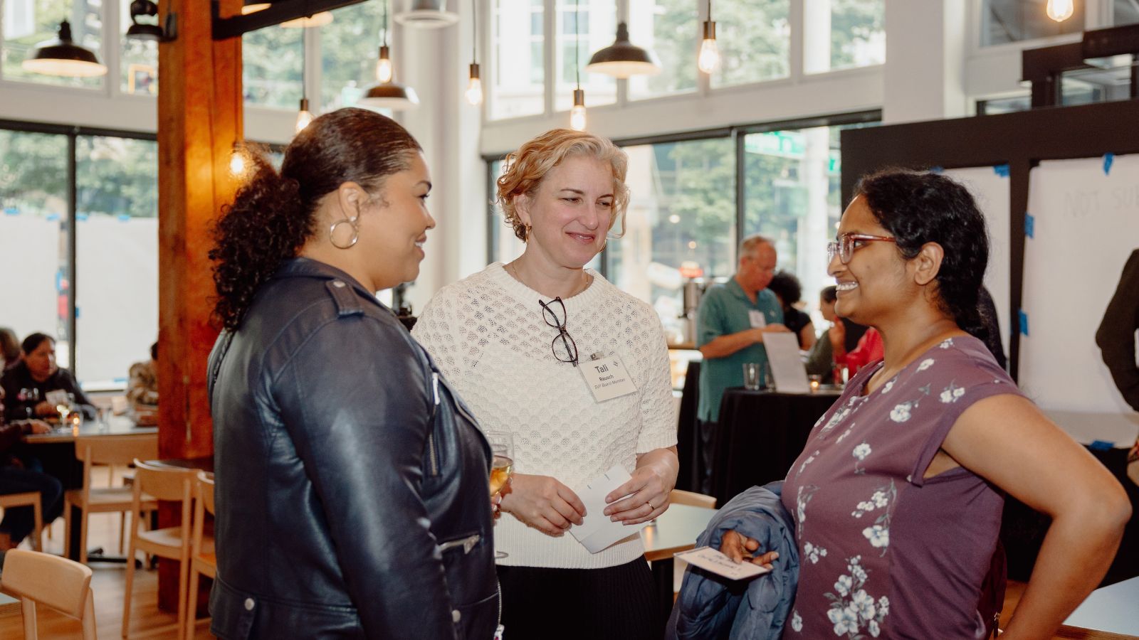 Three participants in SVP Seattle’s Purposeful Philanthropy Cohort stand in conversation during an in-person gathering at a light-filled community space in Seattle.