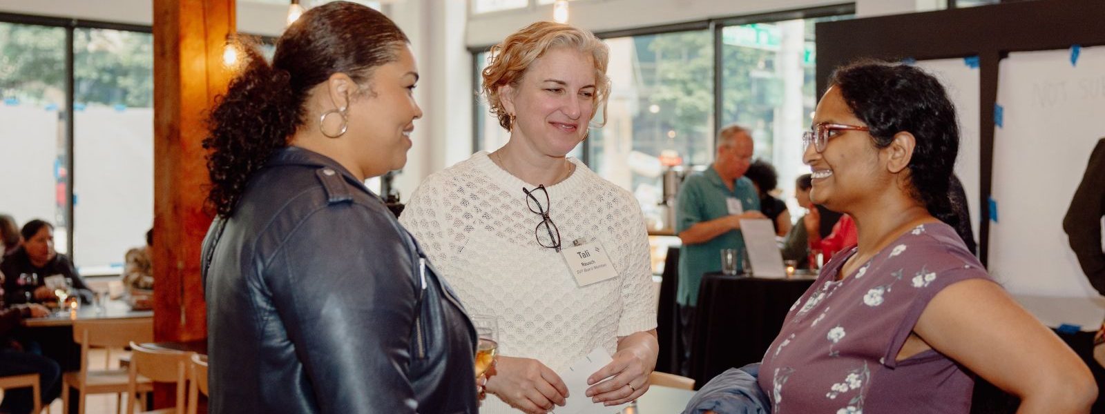 Three participants in SVP Seattle’s Purposeful Philanthropy Cohort stand in conversation during an in-person gathering at a light-filled community space in Seattle.